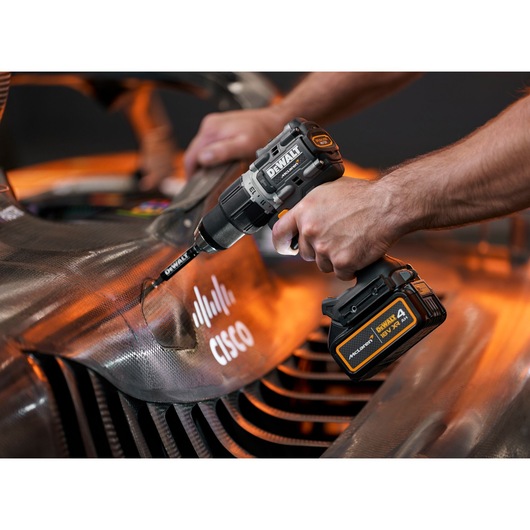 Close-up of a person using a DEWALT cordless drill to work on a car part with a Cisco logo. The drill features a DEWALT