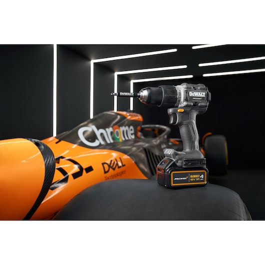 DEWALT cordless drill displayed on a tire with an orange race car in the background and LED lights overhead.