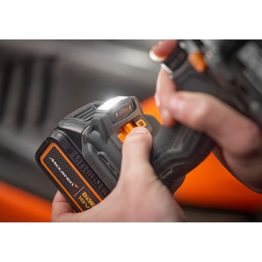 Hand adjusting settings on a DEWALT 18V cordless tool with a lit LED work light.