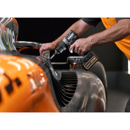 A person using a DEWALT cordless drill on an orange and black race car, focusing on the precise application near the car's