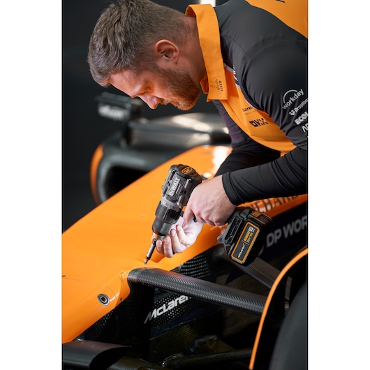 A person in an orange and black uniform uses a DEWALT DCD85MP2T cordless drill to work on the front section of an orange