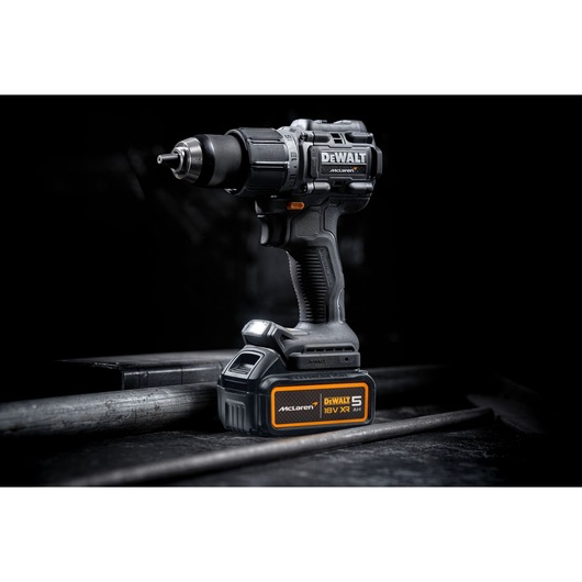 DEWALT 18V XR cordless drill with McLaren branding, resting on a metal surface in a dark studio setting.
