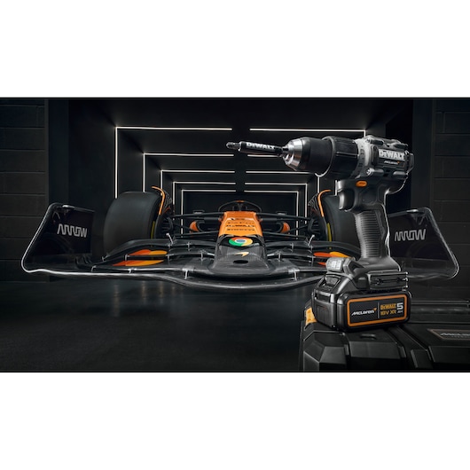 DEWALT power drill in front of an orange race car, both placed in a modern, illuminated garage setting.