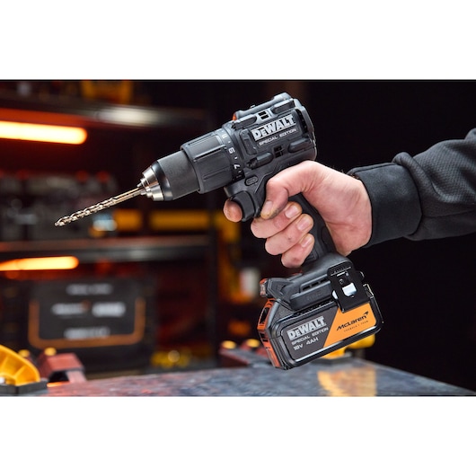 Person holding a DEWALT cordless drill with special edition battery, drill bit attached, in a workshop setting.