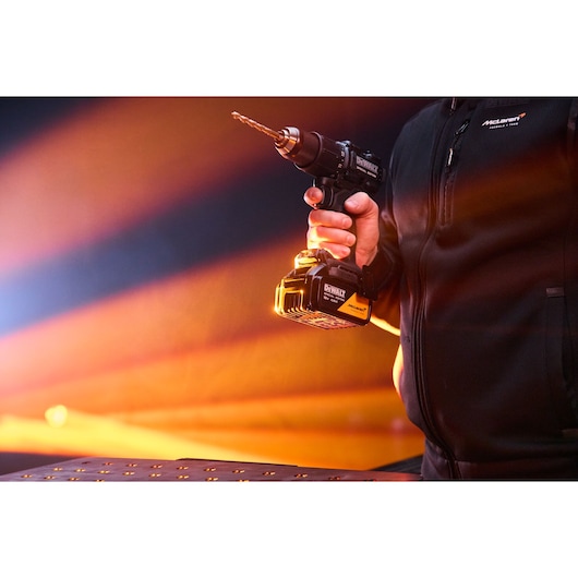 Person holding a DEWALT cordless drill with McLaren branding in front of a brightly lit background.