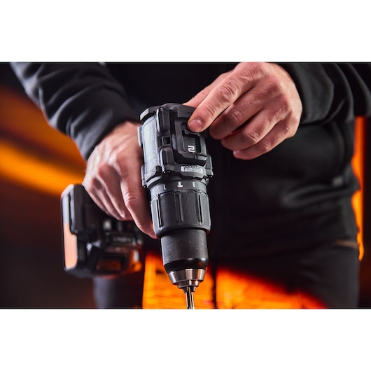Close-up of hands holding and adjusting a DEWALT cordless drill with a glowing orange background.