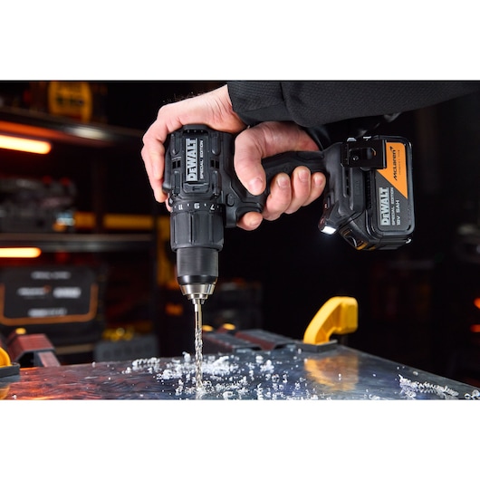 A close-up of a person using a DEWALT cordless drill to drill through a metal surface. Metal shavings are scattered around