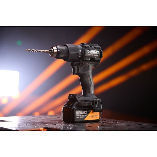 Cordless DEWALT drill with special edition markings, placed on a metal surface with orange lights in background.