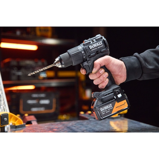 Hand holding a DEWALT DCD86MP1T cordless drill with McLaren special edition battery in workshop setting.