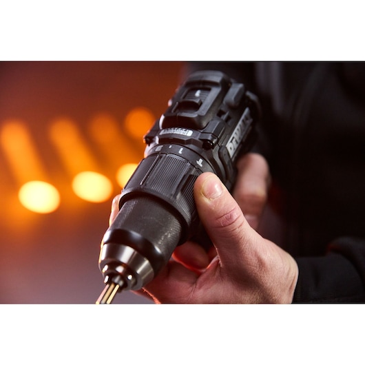 Close-up of a person holding a DEWALT power drill with orange blurred lights in the background.