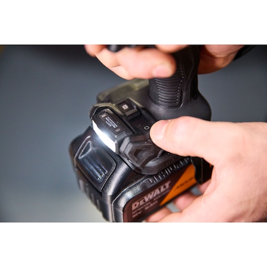 Close-up of hands operating a DEWALT power tool with LED light turned on.