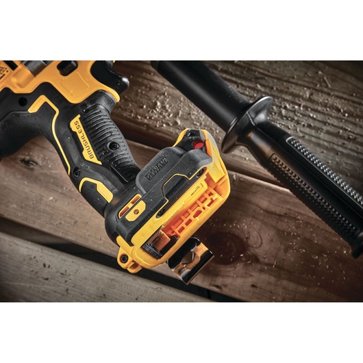 Close-up view of a DEWALT brushless cordless drill, showing the handle, battery attachment area, and a side handle grip, placed on wooden boards.