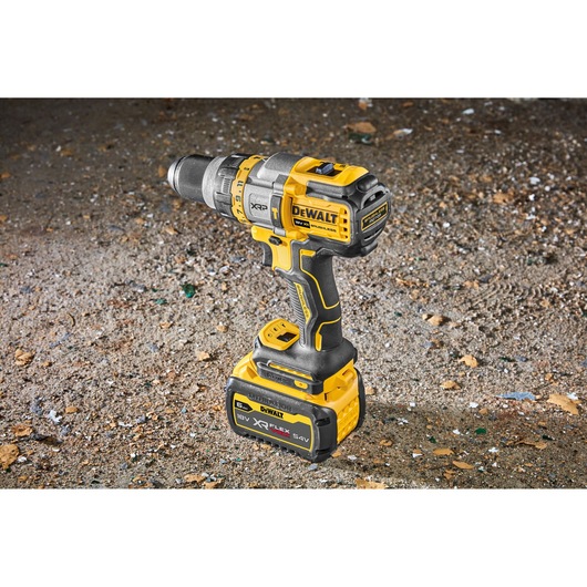 A DEWALT cordless power drill with a yellow and black body, standing upright on a rough surface. The drill features XR FLEXVOLT technology and an 18V battery pack attached at the base.
