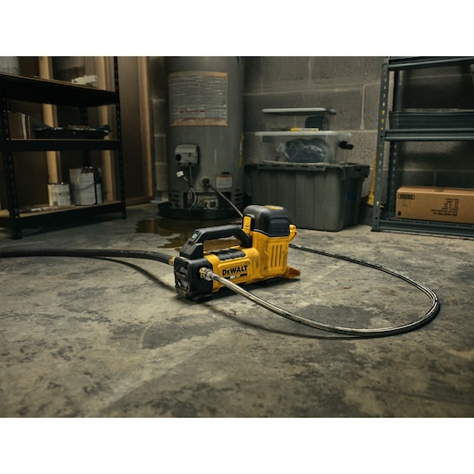 A DEWALT portable cordless water pump sits on the floor in a workshop or utility room, with hoses attached, surrounded by