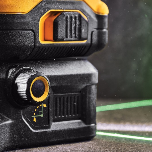 Close-up view of a DEWALT DCE089D1G18 green laser level unit showing its adjustment knob, yellow and black casing, and a visible green laser line projected across the surface.
