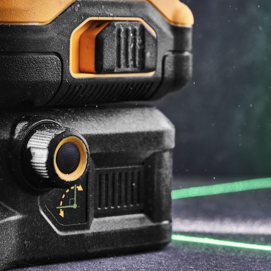 Close-up of a DEWALT green laser level tool, showing its adjustment knob, battery area, and a visible green laser line projected on a surface.