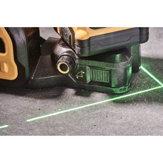 Close-up of a DEWALT laser level tool emitting bright green laser lines on a concrete surface, showing adjustment knobs and construction details.