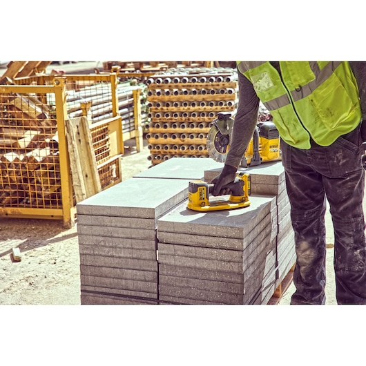 A construction worker uses a DEWALT cordless tool on a stack of concrete slabs at an outdoor construction site. The worker