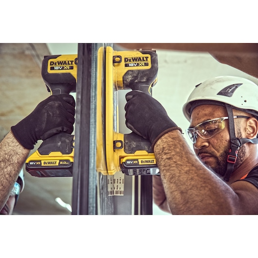 Two people wearing black gloves and safety gear are using DEWALT 18V XR cordless power tools with yellow and black design to