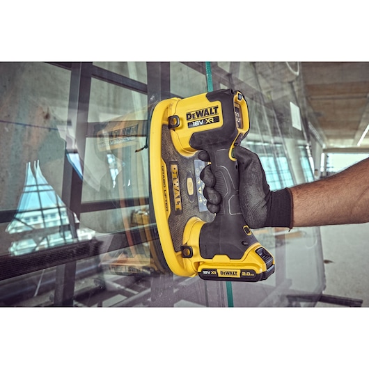 A person wearing a black work glove is using a DEWALT 18V XR glass lifter tool to handle a large sheet of glass on a
