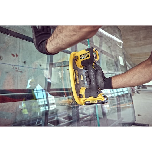 A person wearing black gloves uses a DEWALT DCE590 cordless suction cup tool to handle a sheet of glass in an industrial