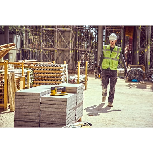 A DEWALT power tool, model DCE590, sits on top of concrete slabs at a construction site. There is a construction worker in a