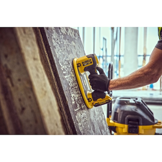 A person wearing a black glove uses a DEWALT DCE590 power tool to work on a large concrete surface at a construction site
