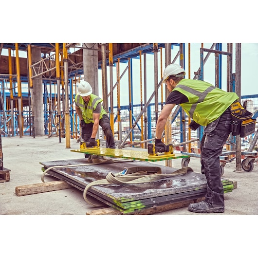 Two construction workers wearing high-visibility vests and hard hats are using DEWALT cordless tools to move a large metal