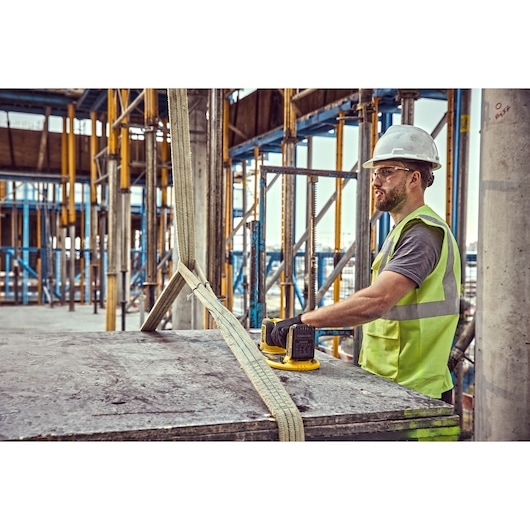 A construction worker wearing a hard hat and a fluorescent safety vest is using a DEWALT tool to handle a large slab secured
