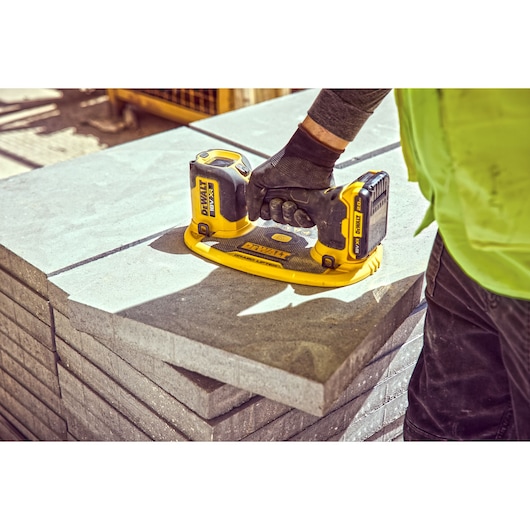 A person in work attire uses a DEWALT cordless tool to lift a large concrete slab on a construction site.