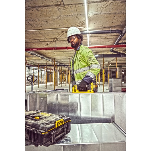 A person wearing a high-visibility jacket and a safety helmet is working on a construction site. The individual is holding a