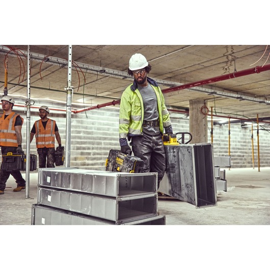 Construction workers in safety gear, including hard hats and reflective jackets, are working at an indoor construction site