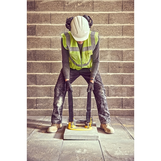 A construction worker wearing a white hard hat, high-visibility vest, gloves, and headphones is using a lifting tool to move