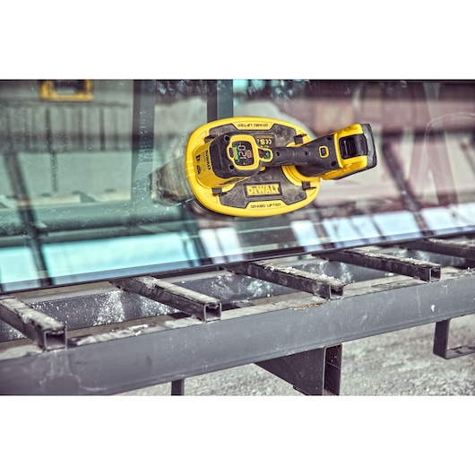 DEWALT glass lifter tool attached to a glass sheet above a metal frame in an industrial environment.