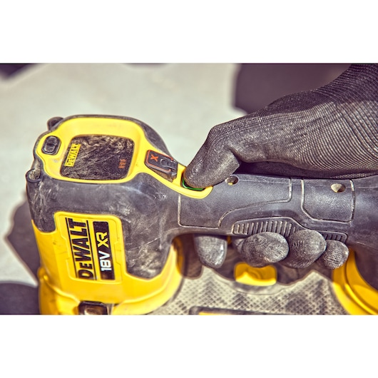 Gloved hand pressing button on a DEWALT 18V XR power tool, close-up of handle and controls.