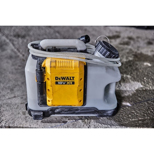 A DEWALT 18V XR portable sprayer with a yellow battery compartment and translucent tank, placed on a concrete surface. A hose and spray nozzle are attached to the unit.