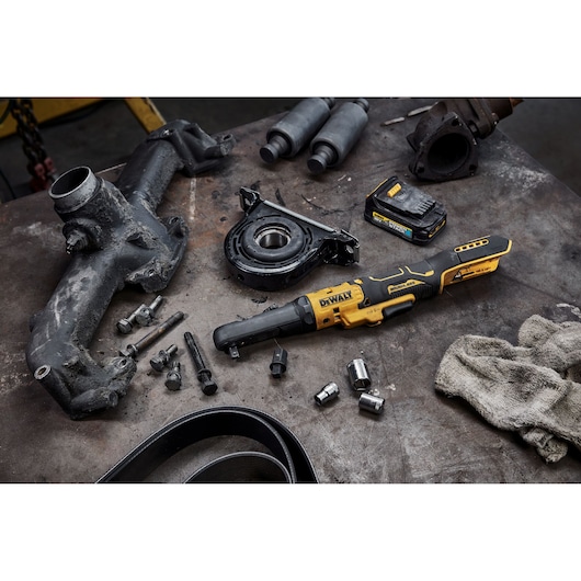 DEWALT cordless ratchet tool with battery, parts, and accessories on a workshop table.