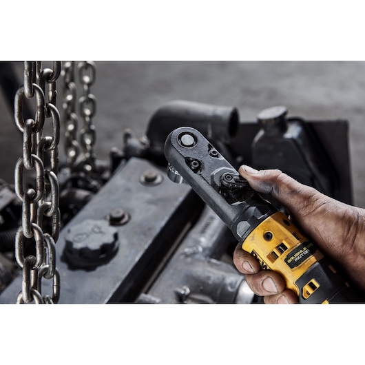 Hand holding DEWALT ratchet tool near machinery and metal chains in an industrial setting.