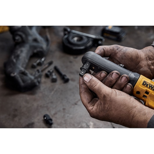 Hands holding a DEWALT ratchet tool, with bolts and parts visible on a workshop surface in the background.