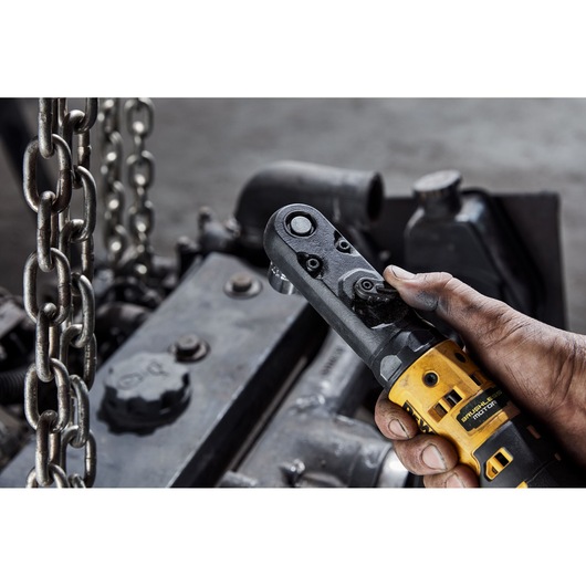 Hand holding a yellow DEWALT ratchet tool near metal parts and chains in an industrial setting.