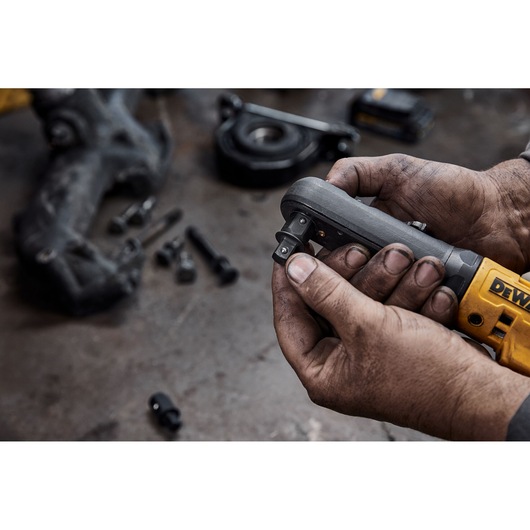 Hands holding a DEWALT cordless ratchet tool, with bolts and parts on a workshop table.