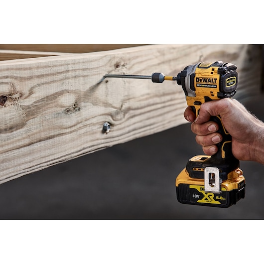 A person using a DEWALT DCF850NT cordless impact driver to drive a screw into a piece of wood.