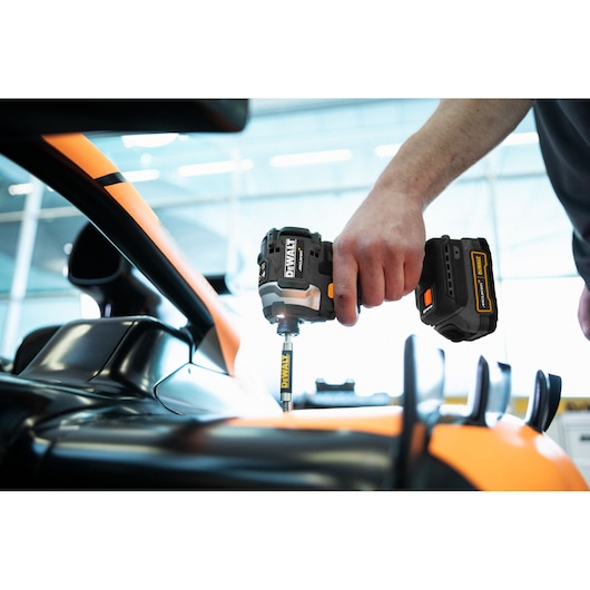A person using a DEWALT cordless impact driver to fasten or remove a screw on a sleek, orange and black automotive component.