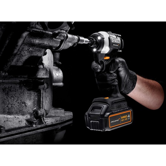 A person uses a DEWALT cordless impact driver to tighten a bolt on a metal machine part, wearing a black glove.