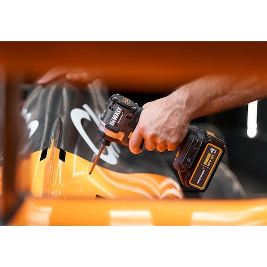 Hand using a DEWALT cordless impact driver on a black and orange surface.