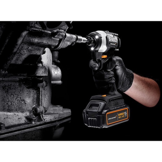 DEWALT cordless impact driver being used on metal machinery by a gloved hand, close-up view.