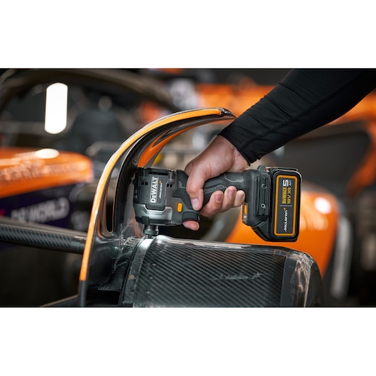 A person uses a DEWALT cordless tool on a carbon fiber part of an orange racing vehicle.
