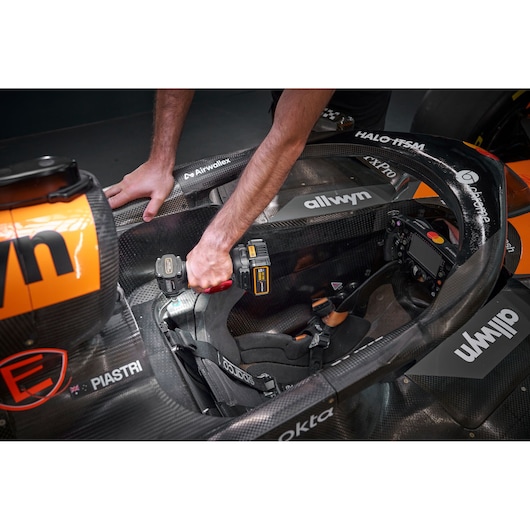 Person using a DEWALT tool inside a race car cockpit, working near the seat and steering area.