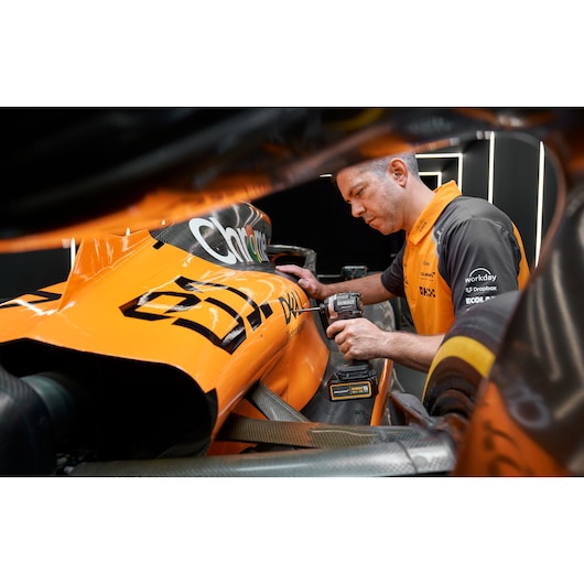 Person uses a DEWALT tool on an orange race car, focusing on maintenance or assembly work.