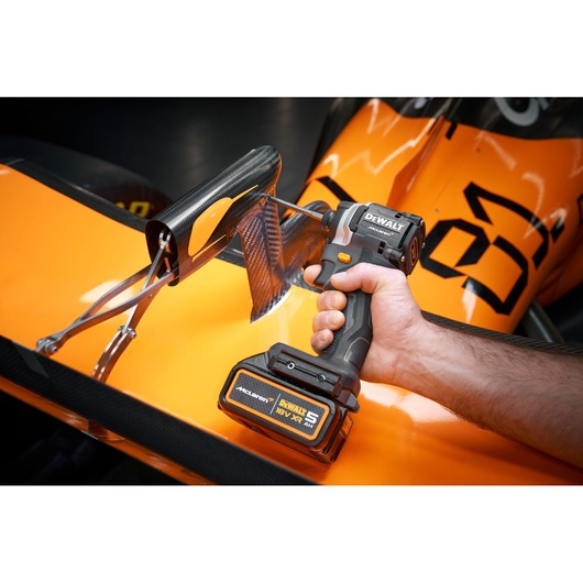 A DEWALT cordless drill used on an orange race car part, held by a person's hand.